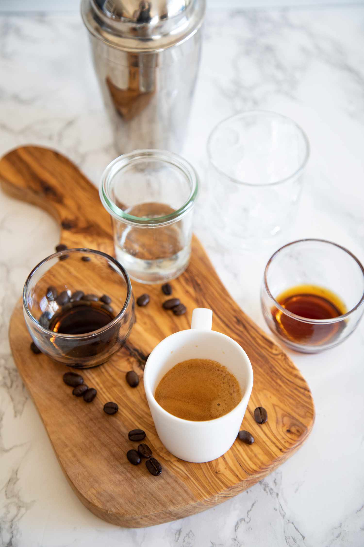 Ingredients for an Espresso Martini Cocktail with espresso beans and glasses on a wooden serving board.