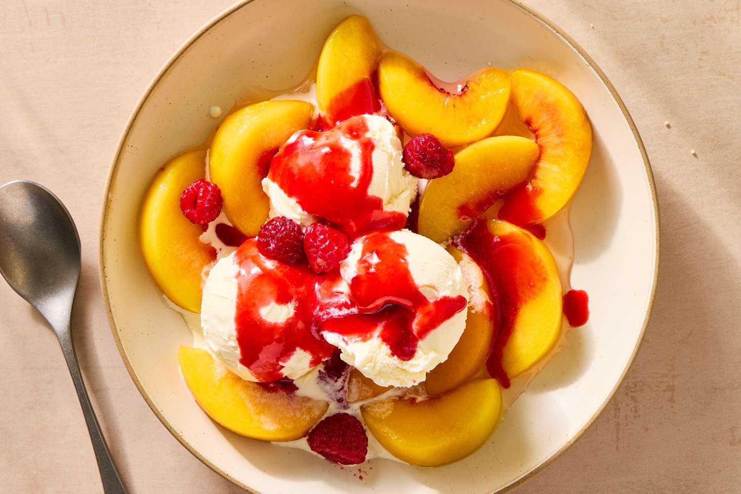 A dish of sliced peaches with scoops of ice cream, raspberries, and red sauce