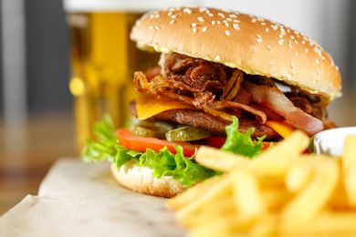 A close-up view of a gourmet hamburger with fries and a glass of beer in the background