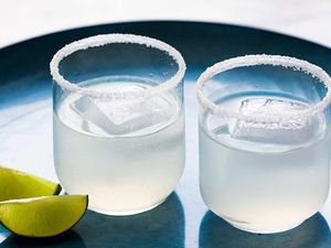 Two classic margaritas in glasses with salted rims and lime wedges off to the side