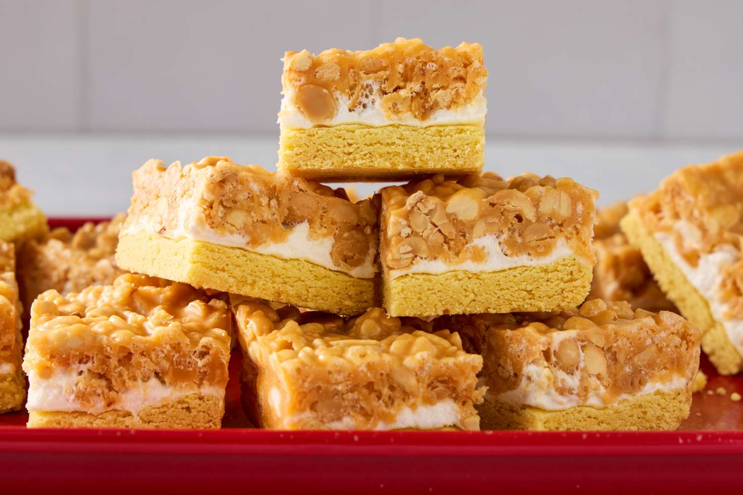 A stack of salted nut roll bars on a red tray featuring layers of a baked base marshmallow center and nut topping
