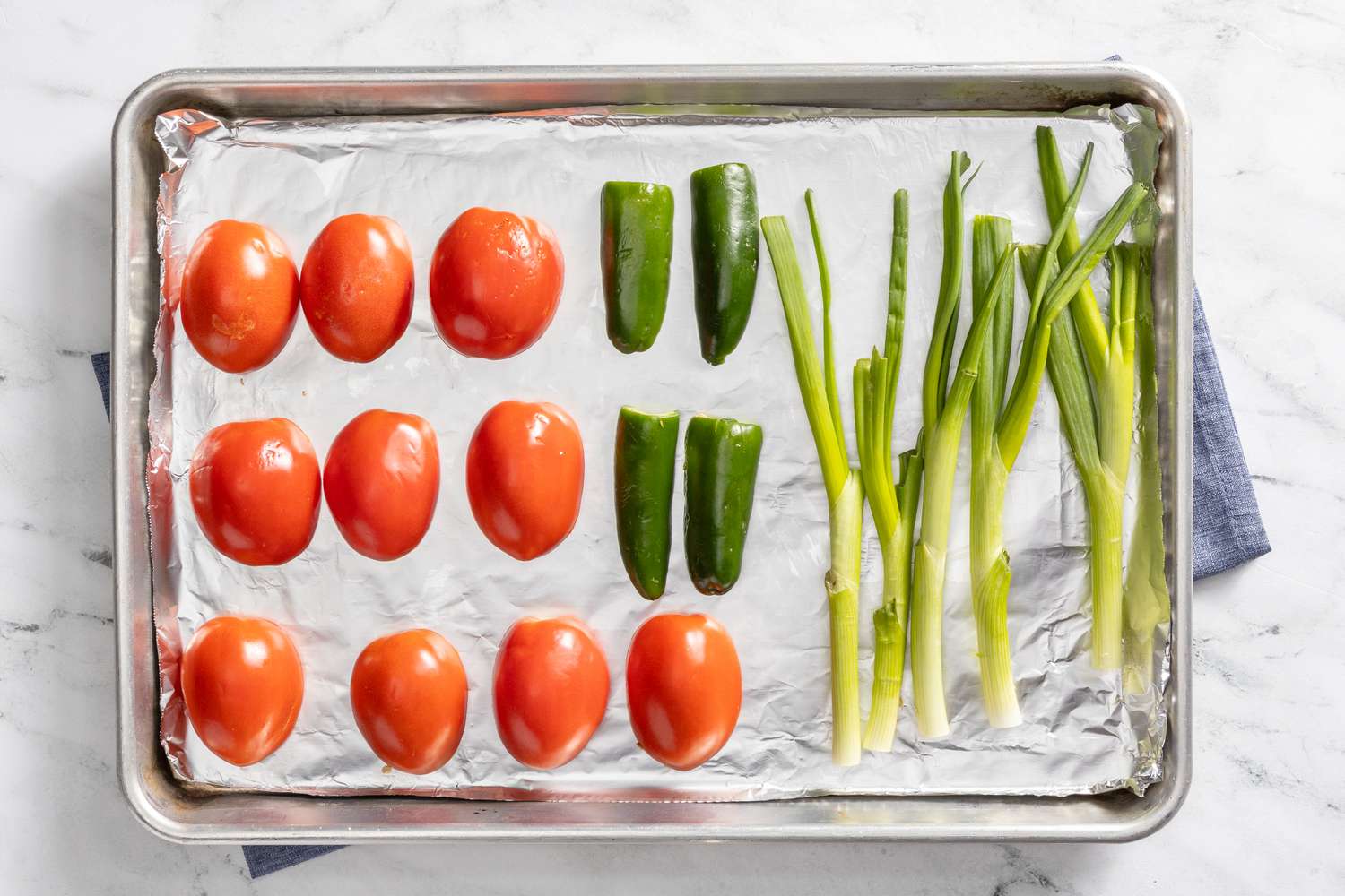 tomatoes, jalapenos, and green onion on an aluminum foil-lined baking sheet for borracho beans (frijoles beans) recipe