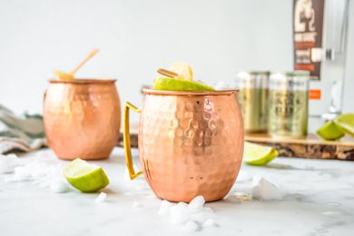 Mezcal Mule in Two Copper Mugs Surrounded by Ice and Limes. More Ingredients in the Background