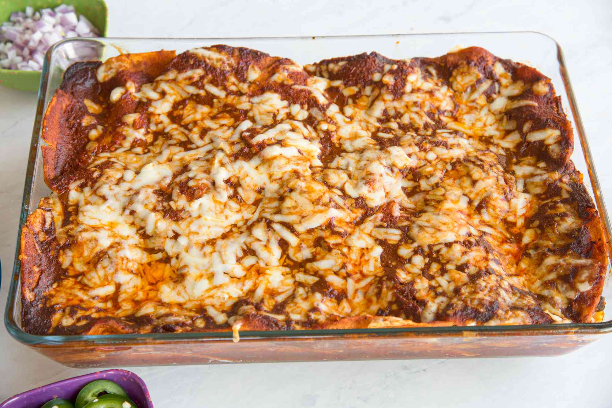 Easy Chicken Enchilada Casserole in a Casserole Dish Next to a Bowl with Chopped Onions and Sliced Jalapenos