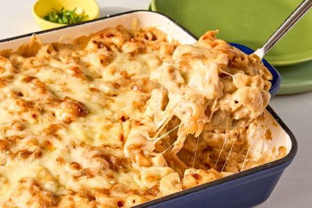 A casserole dish with cooked French onion mac and cheese some being lifted out with a serving utensil