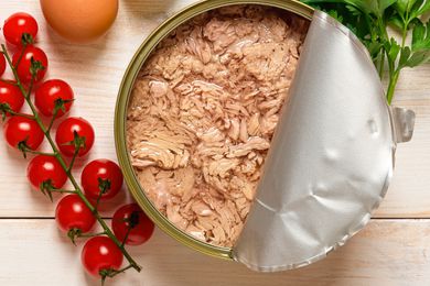 A halfway open can of oil-packed tuna. There are cherry tomatoes, an egg, and parsley next to the can.