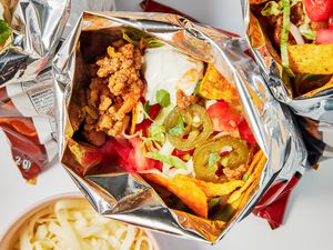 Bags of walking tacos with toppings on the counter next to a bowl of shredded mozzarella