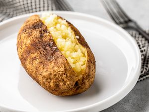 Opened Grilled Baked Potato on a Plate Next to a Fork and Napkin