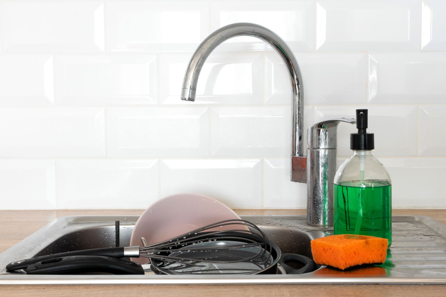 Kitchen sink with a faucet dish soap a sponge and utensils in the basin