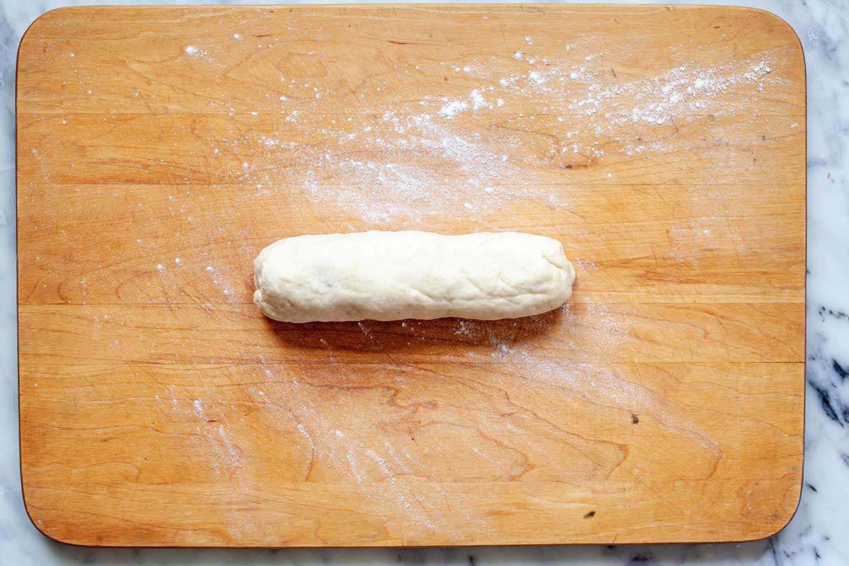 Dough for easy homemade flour tortillas is shaped like a log in the middle of a wooden cutting board.