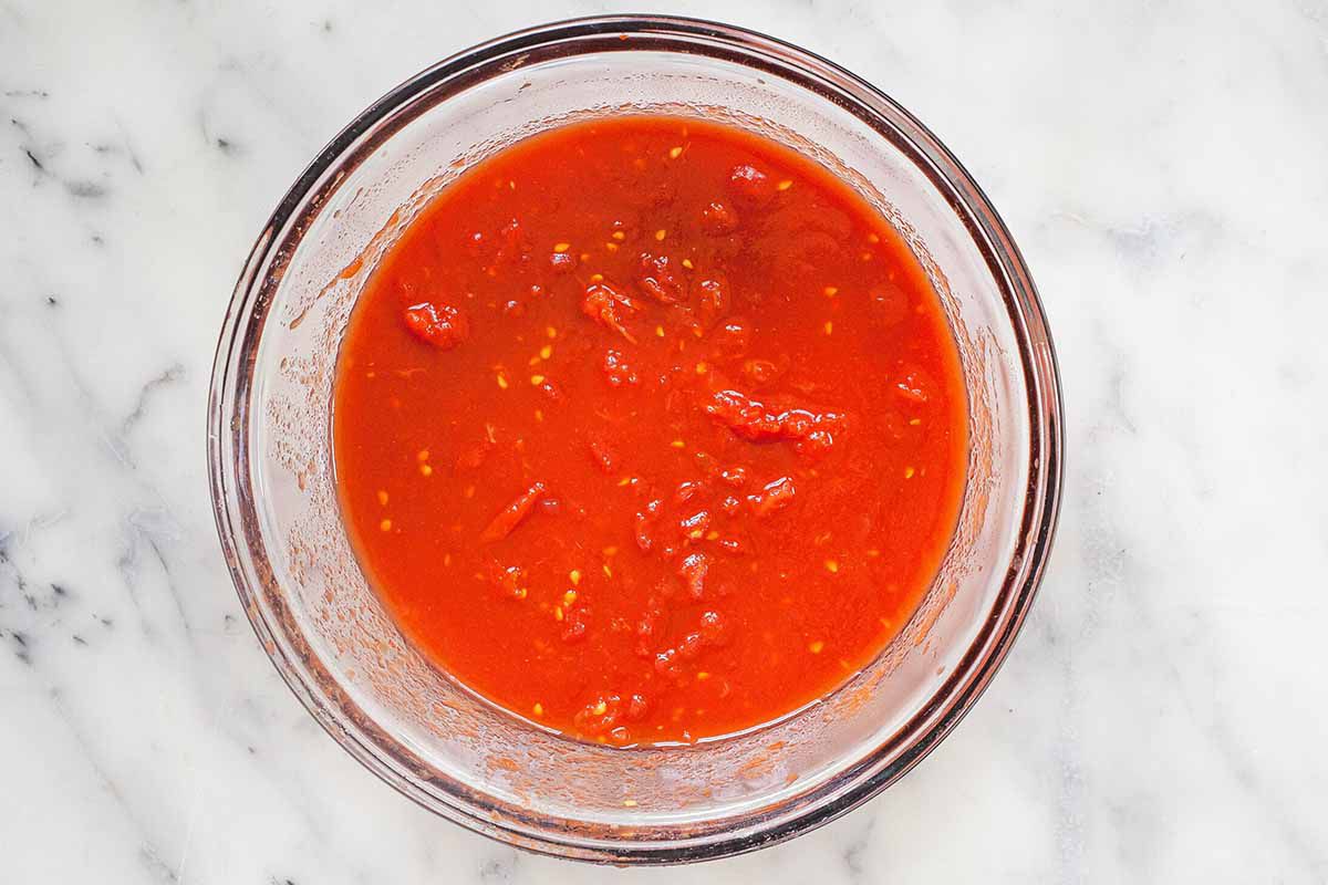 Tomatoes being crushed in a bowl to make the best pasta sauce recipe.