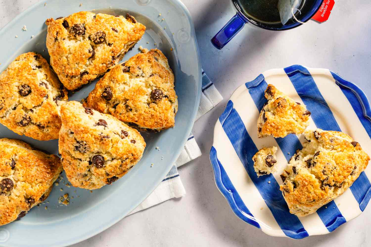 A platter and plate of chocolate chip scones served with a cup of tea