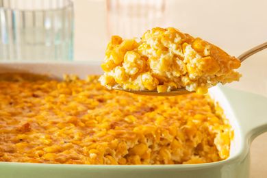 Spoonful of corn pudding lifted from a casserole dish with more