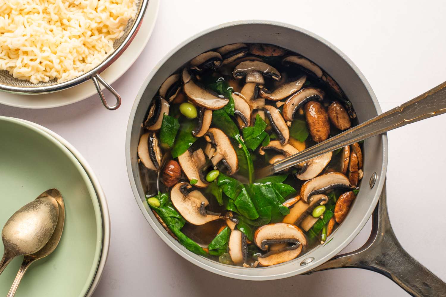 A pot of mushroom noodle soup next to a plate of rice