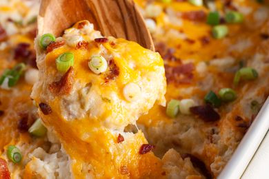 A wooden spoon lifting a serving of twice baked potato casserole from a baking dish