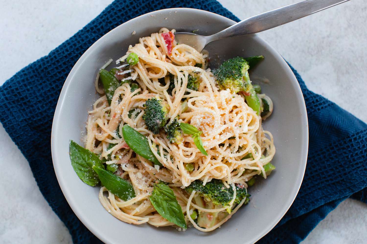 Overhead view of primavera pasta in a bowl with a navy linen underneath.