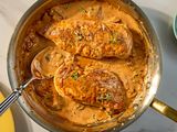 Two cooked chicken breasts in a creamy sauce in a skillet garnished with herbs