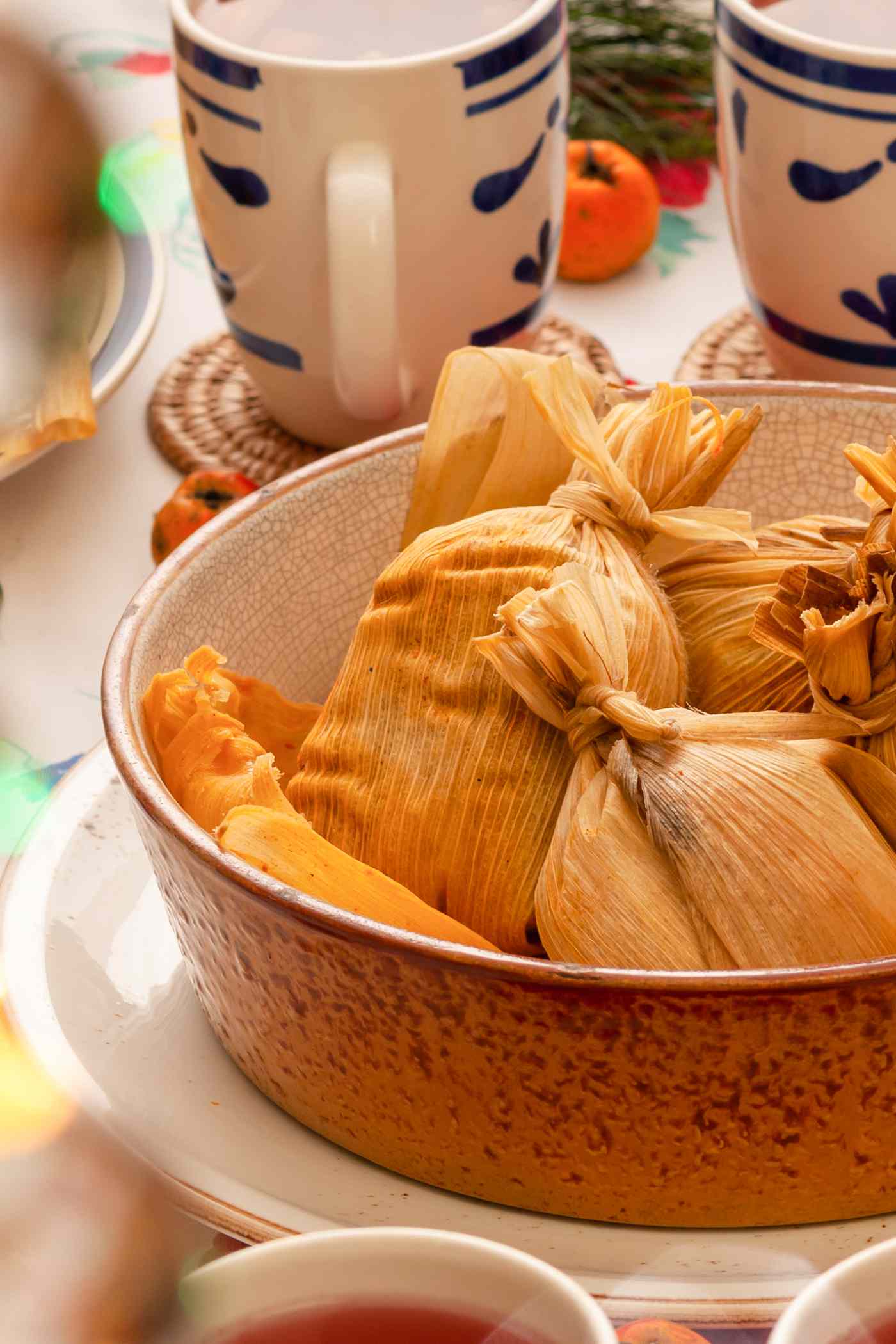 Tamales in a bowl at a table setting with mugs, plate, and fresh fruit