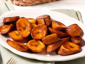 Maduros (Fried Sweet Plantains) on a Plate, and in the Surroundings, a Light Olive Green Kitchen Towel and a Woven Basket