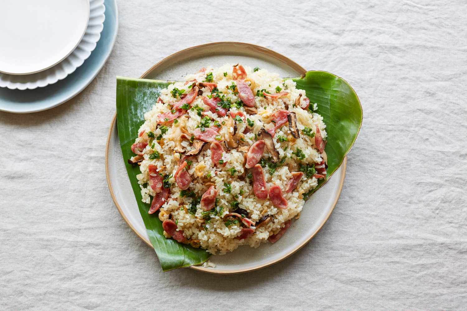 Steamed rice with sausage, dried shrimp, and mushrooms served over banana leaves and with three smaller plates set by it.