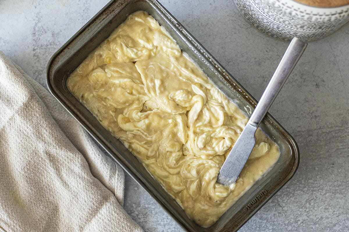 Unbaked homemade cream cheese banana bread in a pan with a butter knife swirling the batter.
