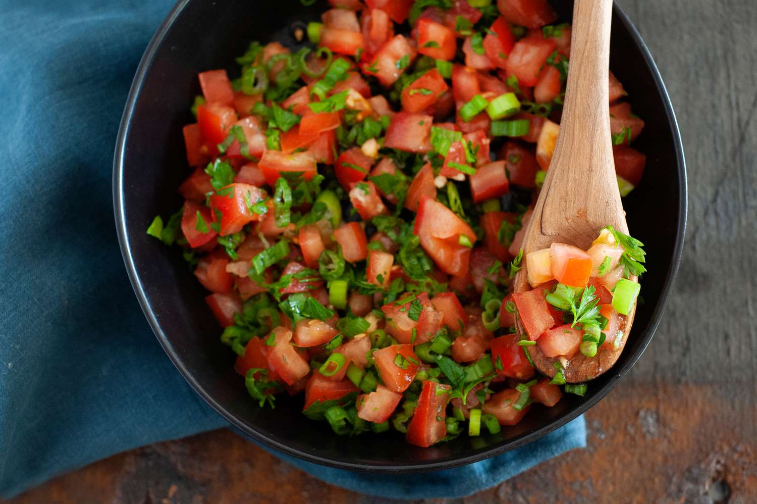 Overhead view of East African Tomato Relish in a dark bowl with a wooden spoon lifting up some of the relish.