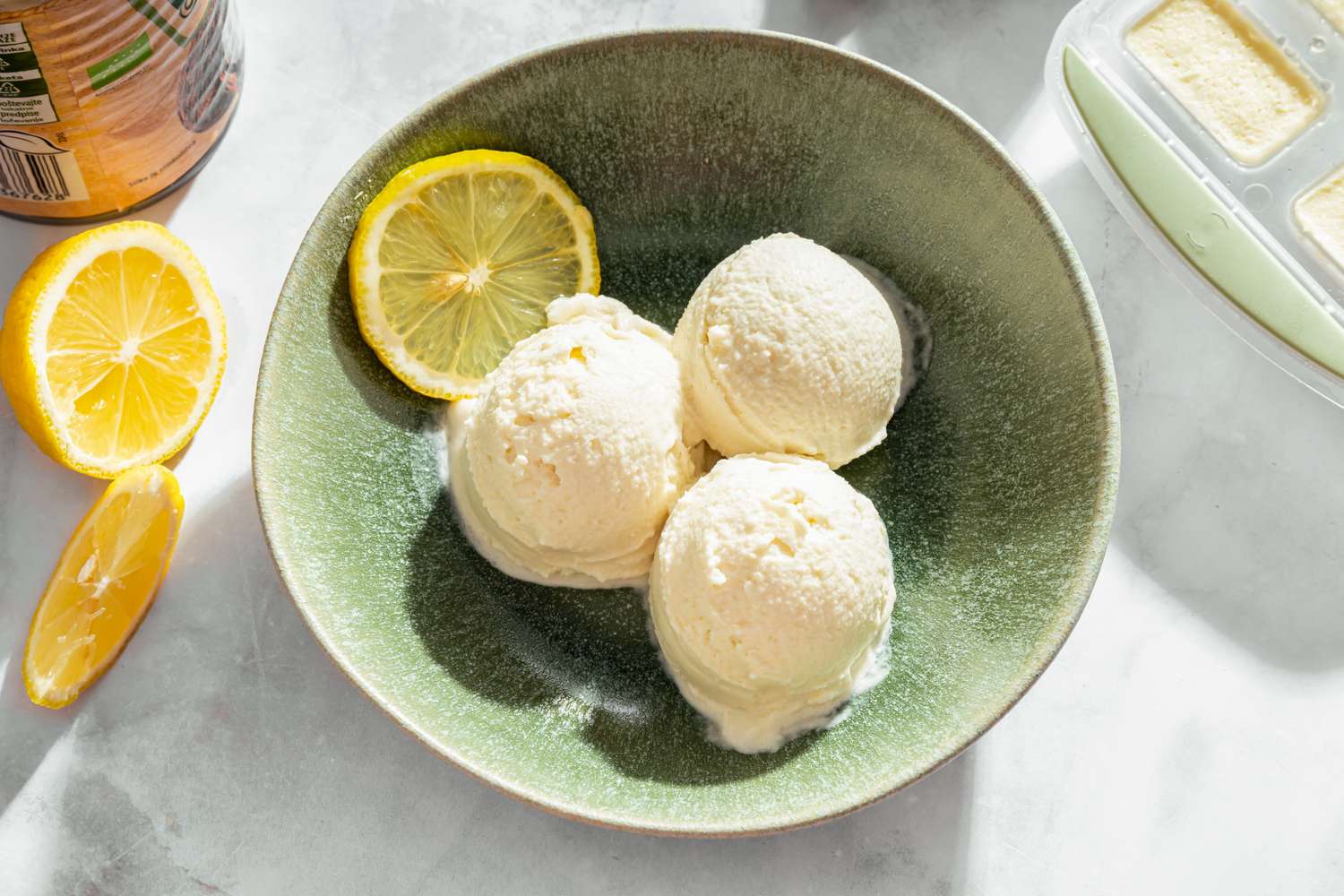 Three scoops of a frozen dessert served in a bowl with slices of lemon placed beside it