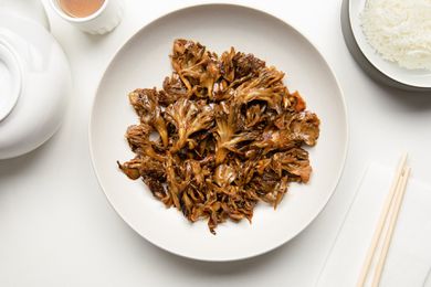 Stir-Fried Maitake Mushrooms with Garlic and Chile Oil in a Plate Next to a Pair of Chopsticks, a Bowl of Rice, a Cup of Tea, and a Tea Kettle