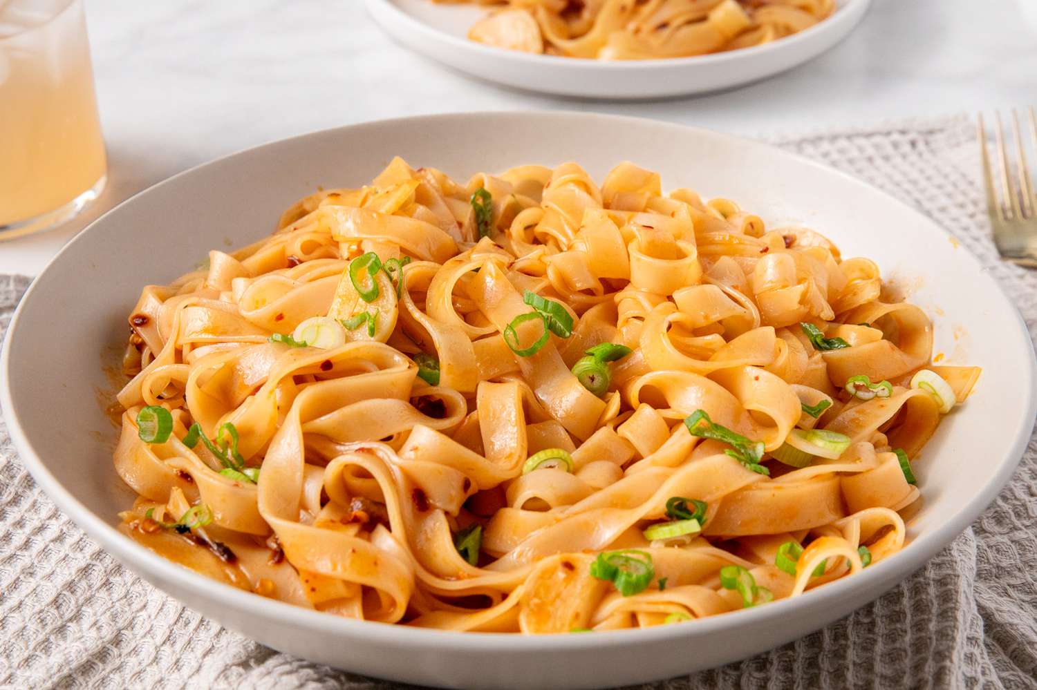 Sideview of a large serving plate with broad rice noodles on a garlic sauce, garnished with sliced scallions