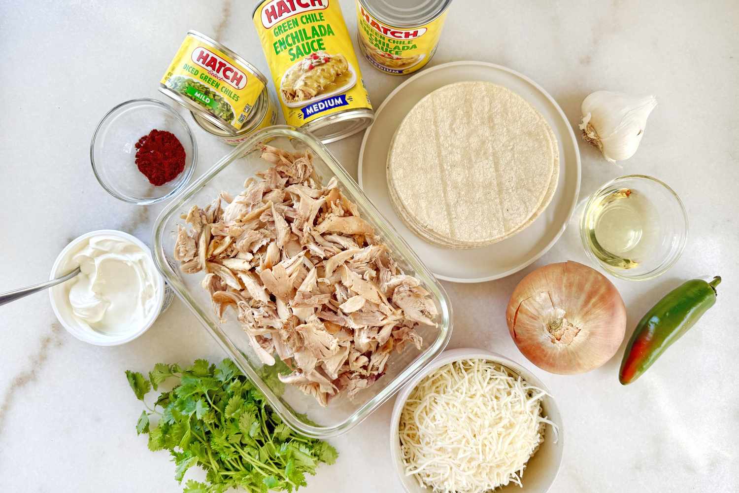 Ingredients arranged for making chicken enchilada casserole including shredded chicken tortillas cheese and various condiments