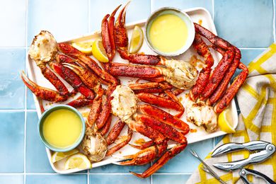 Tray of Easy Baked King Crab Legs With Bowls of Melted Butter and Lemon Wedges, and on the Counter Next to It, a Few Seafood Picks and Cracker on a Table Napkin
