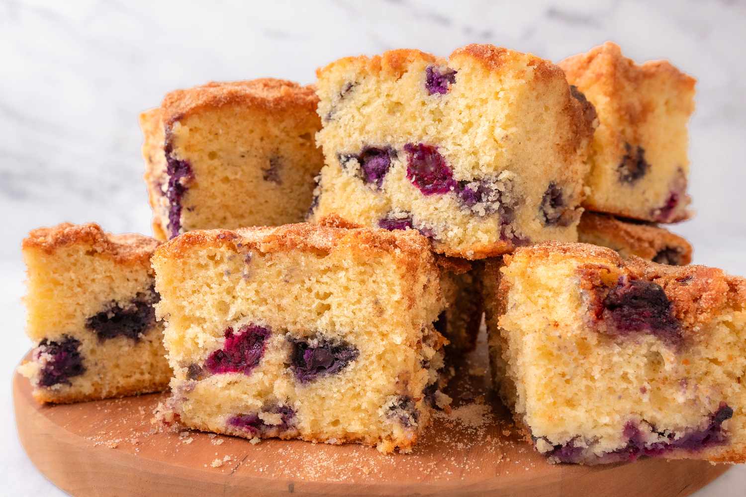 Side view of multiple blueberry coffee cake slices stacked on a wooden cutting board