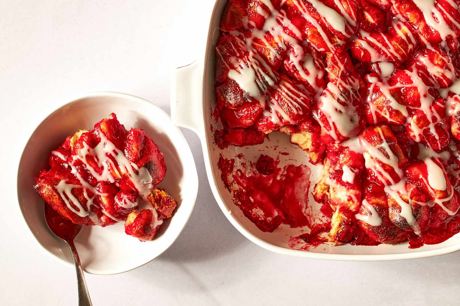 verhead shot of a baking dish with cherry cobbler, with a portion of the cobbler scooped into a bowl
