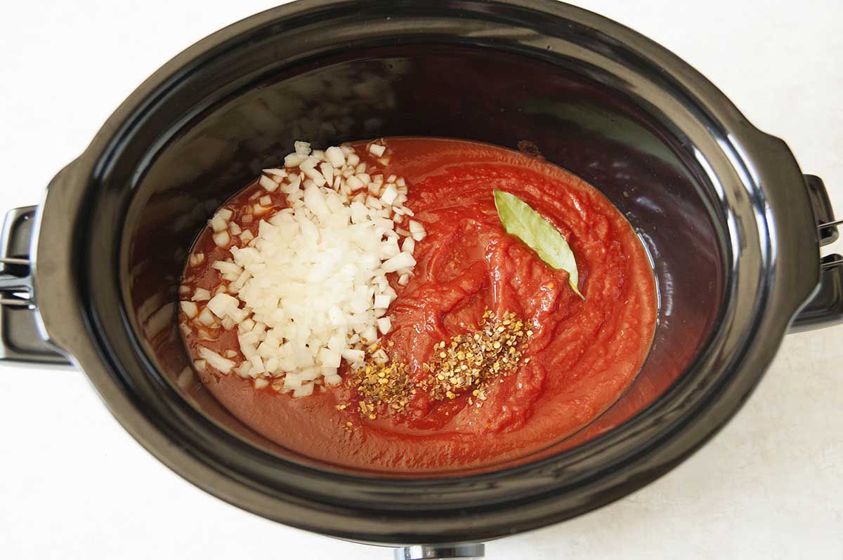 Tomato suace, herbs and onions in a slow cooker for tomato sauce with slow cooker meatballs.