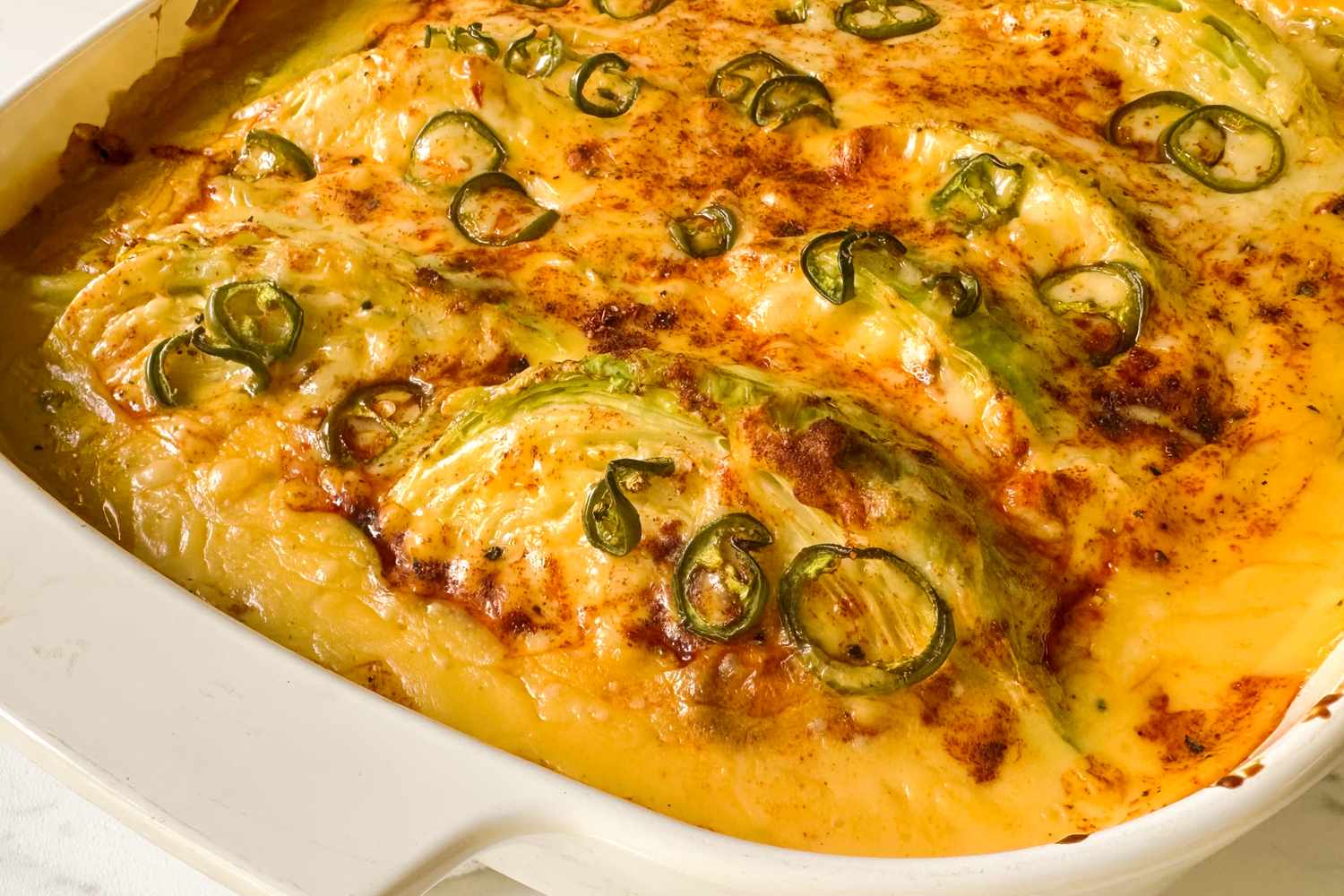 Cheesy baked cabbage topped with sliced jalapeos in a white casserole dish