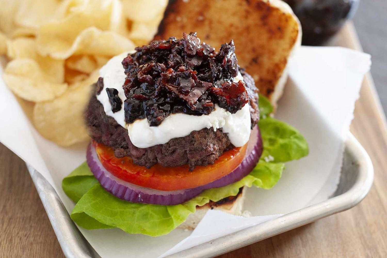 Hamburger with toppings including bacon jam lettuce tomato and onion with chips on the side