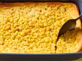 dark blue baking dish of corn soufflé with a spoon scooping out a serving