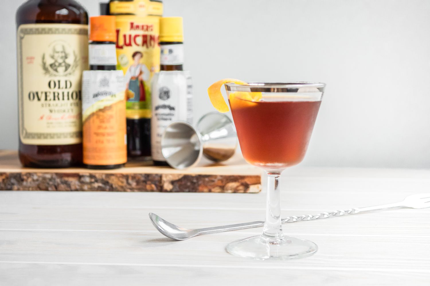 Black Manhattan with an Orange Peel and in the Background, Ingredients on a Wooden Board