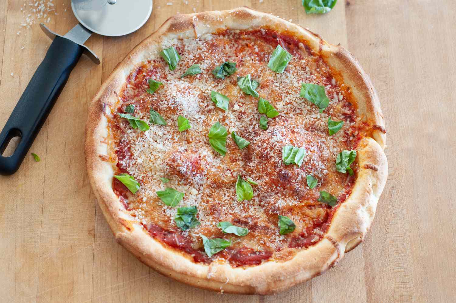 Top pizza with basil on cutting board.