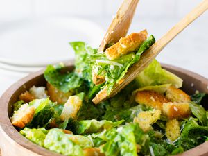Serving Utensils Picking up Some Classic Caesar Salad Topped with Homemade Croutons