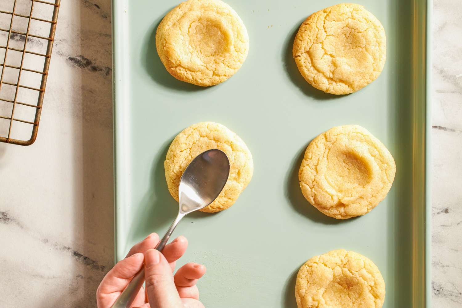 Cookies on a baking tray being shaped with a spoon by a hand