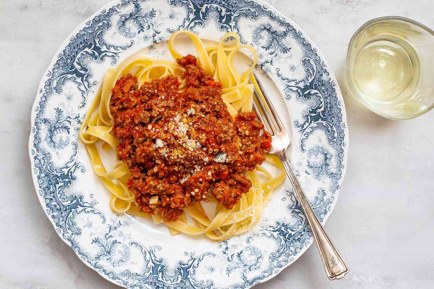 A beautiful fast bolognese sauce on a blue patterned plate with noodles and fork.