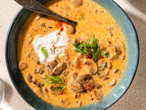 A bowl with Hungarian mushroom soup, topped with sour cream, fresh dill, and smoked paprika