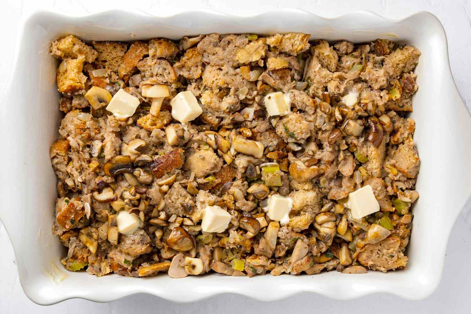 Vegan Mushroom Stuffing Added to Casserole Dish and Topped with More Margarine 