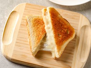 Grilled cheese sandwich on a wooden board cut into triangles with melted cheese oozing out