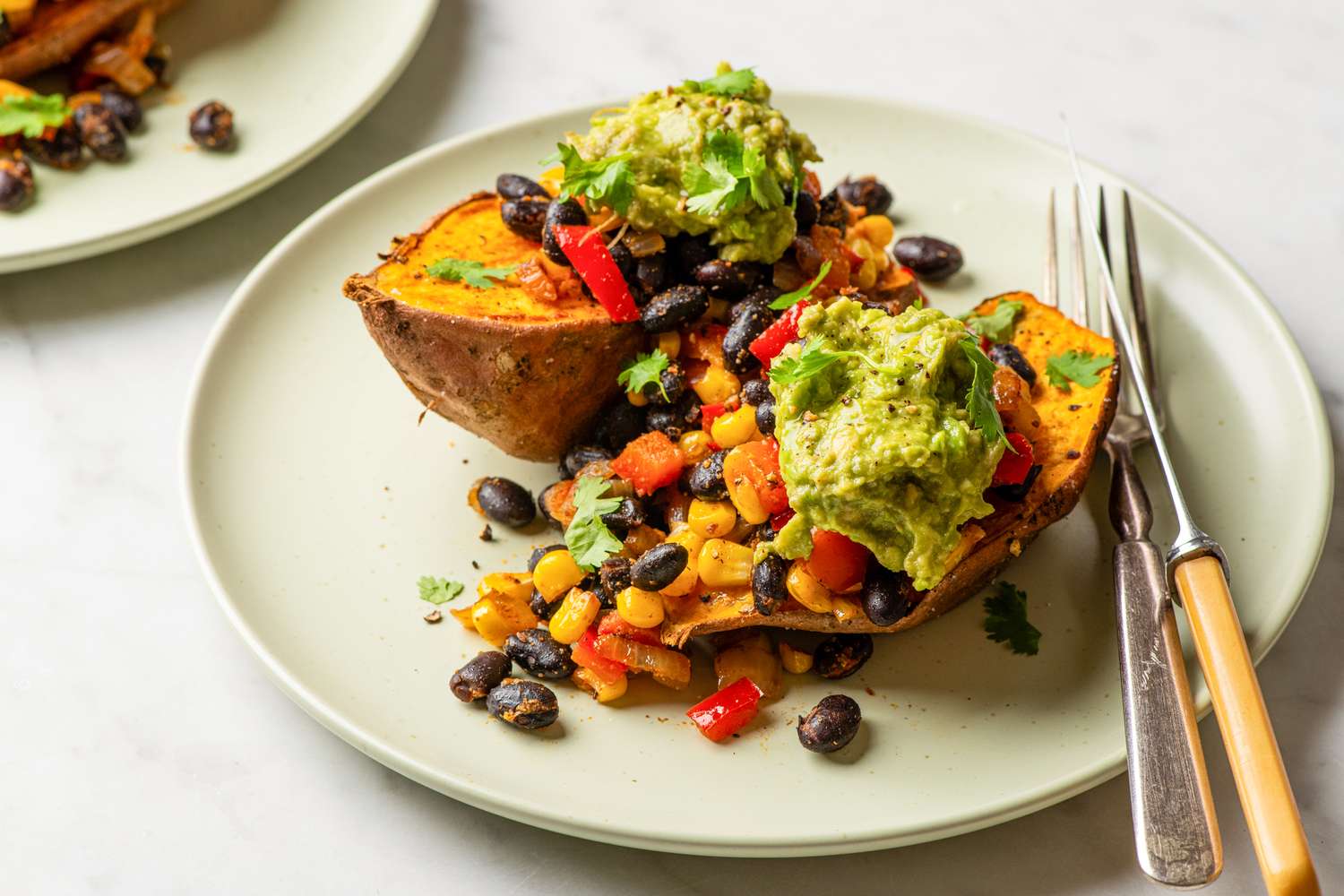 Sweet potatoes topped with black beans corn and guacamole garnished with cilantro on a plate