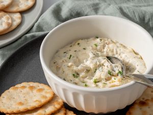 Side view of a bowl of hot crab dip with a spoon and round crackers.