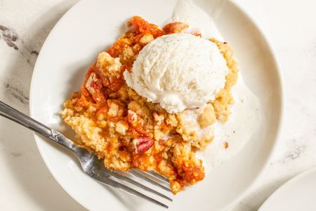 Plate with a serving of pumpkin dump cake topped with a scoop of ice cream fork placed on the side