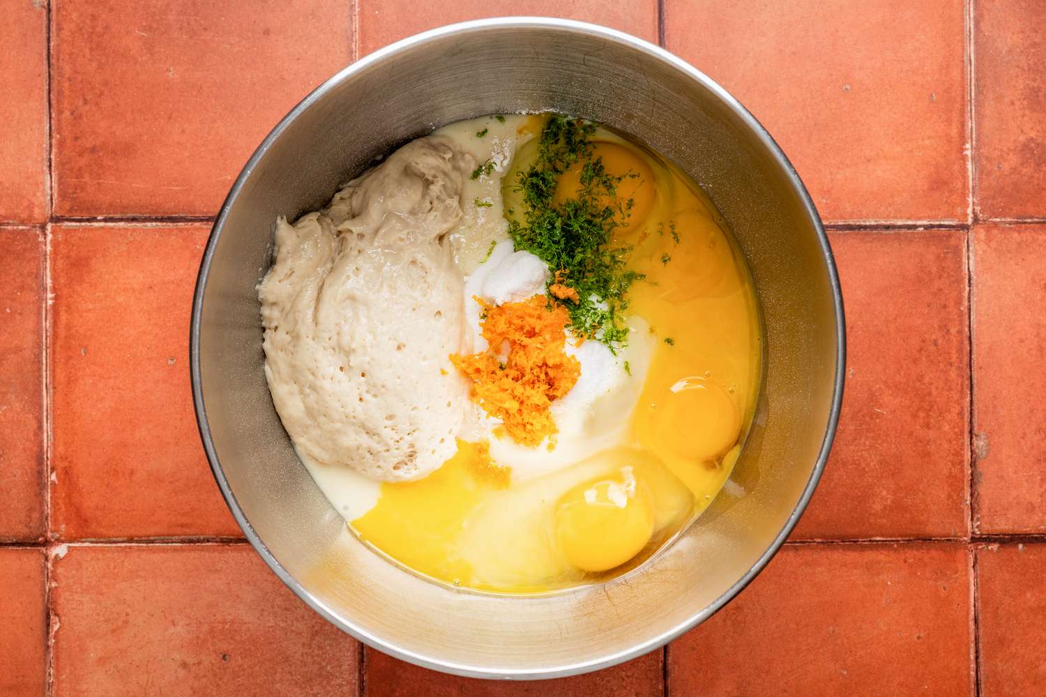 Pan de muerto ingredients in a mixer bowl (eggs, starter, flour, citrus zest, and sugar)