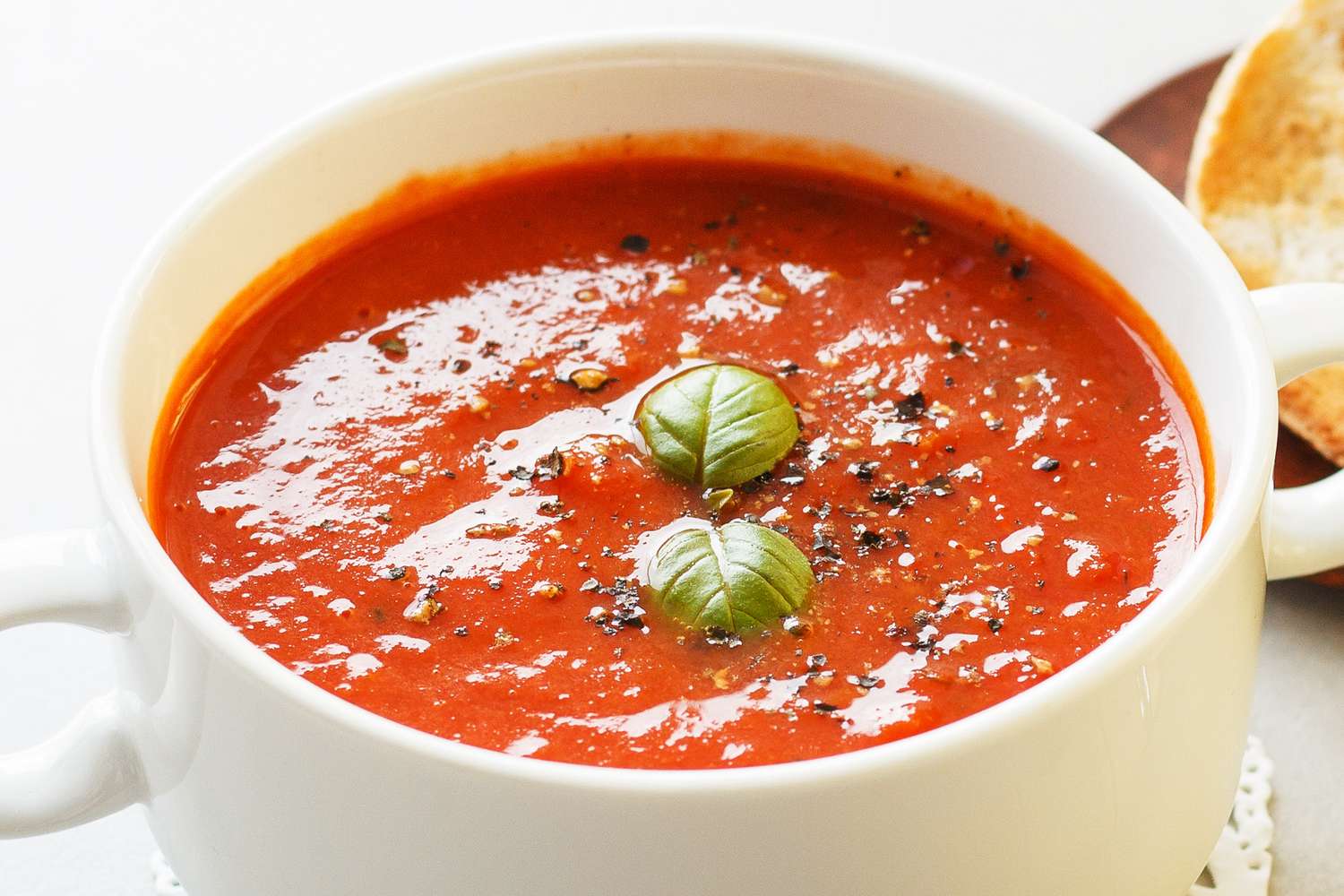 A bowl of tomato soup garnished with basil and cracked black pepper